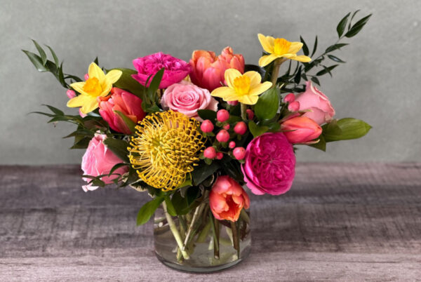 Marmee's Courage is a bold mix of hot pink, yellow, and punch-hued blooms in a glass vase