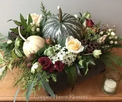 White and green pumpkins mixed with roses and other flowers in a wooden box